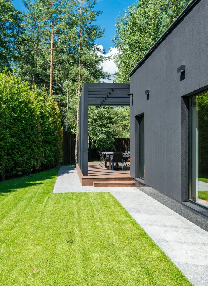Exterior of a renovated modern house with clean lawns, hedges, decking and large glass windows